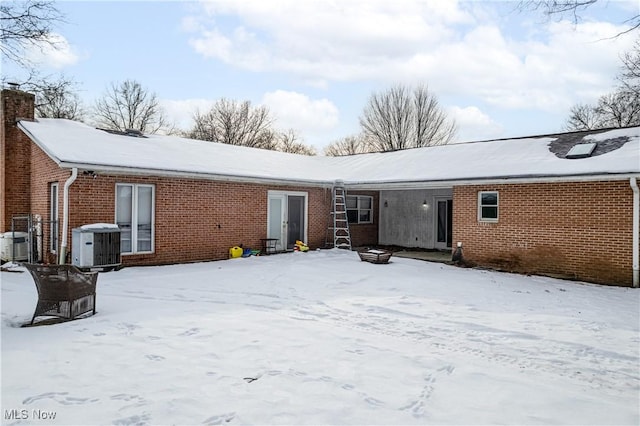 snow covered rear of property featuring central AC