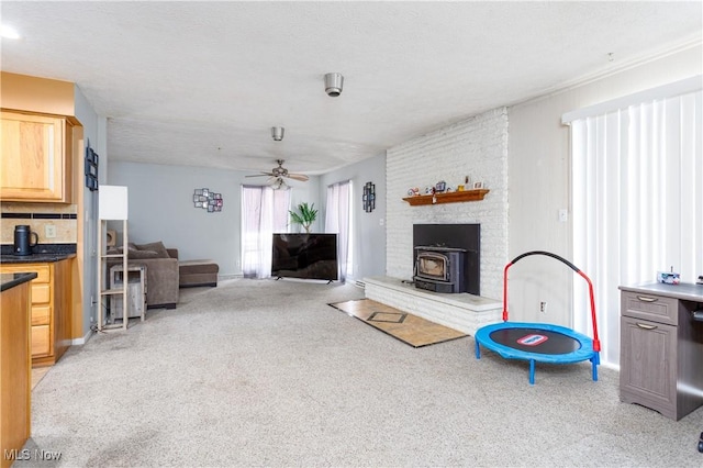 living room with a wood stove, light carpet, a textured ceiling, and ceiling fan