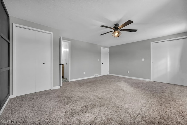 unfurnished bedroom featuring multiple closets, carpet, a textured ceiling, and ceiling fan