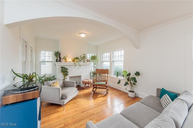 living room with ornamental molding, wood-type flooring, and a brick fireplace