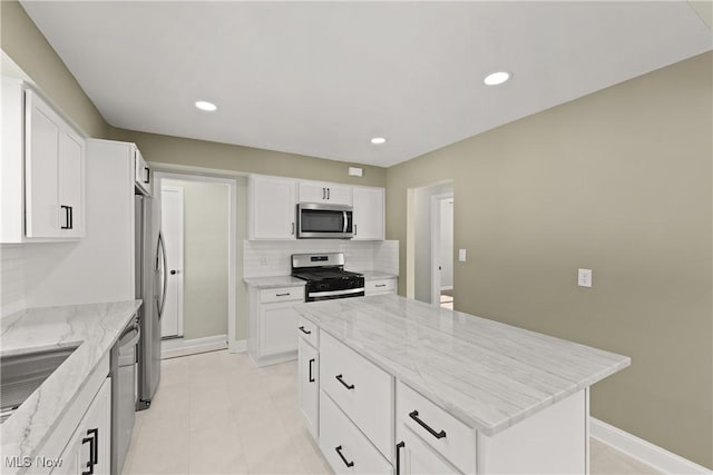 kitchen with appliances with stainless steel finishes, a center island, white cabinets, and light stone counters