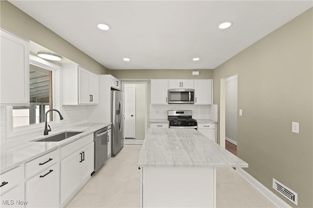 kitchen featuring sink, appliances with stainless steel finishes, white cabinetry, light stone counters, and a kitchen island