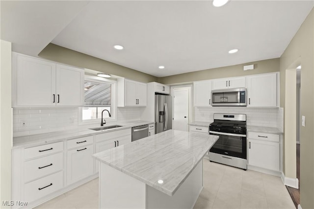 kitchen featuring sink, stainless steel appliances, light stone countertops, white cabinets, and a kitchen island