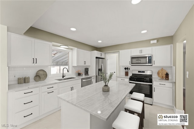 kitchen featuring sink, a kitchen island, stainless steel appliances, light stone counters, and a kitchen bar