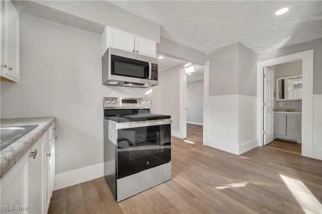 kitchen with appliances with stainless steel finishes, light wood-type flooring, a textured ceiling, and white cabinets