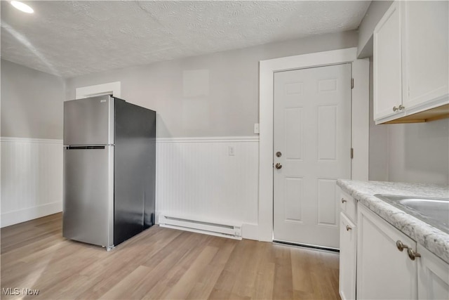 kitchen featuring light hardwood / wood-style flooring, white cabinets, stainless steel refrigerator, and baseboard heating