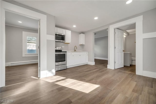 kitchen featuring appliances with stainless steel finishes, hardwood / wood-style floors, a baseboard radiator, sink, and white cabinets