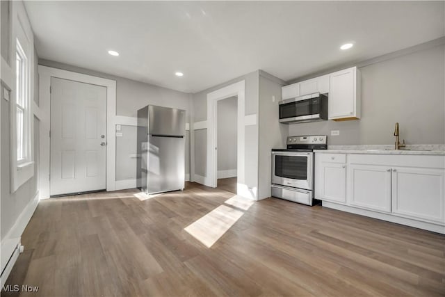 kitchen with white cabinetry, sink, light stone counters, stainless steel appliances, and light wood-type flooring