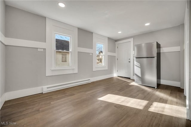 unfurnished bedroom with a baseboard radiator, wood-type flooring, and stainless steel refrigerator