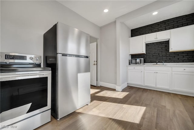 kitchen with tasteful backsplash, white cabinetry, sink, stainless steel appliances, and light wood-type flooring