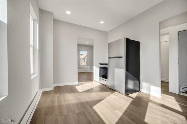 interior space with a baseboard radiator, light wood-type flooring, range, and stainless steel refrigerator