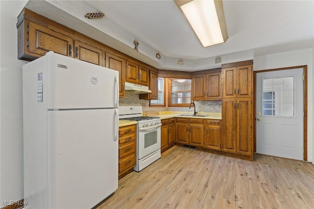 kitchen with sink, decorative backsplash, white appliances, and light wood-type flooring