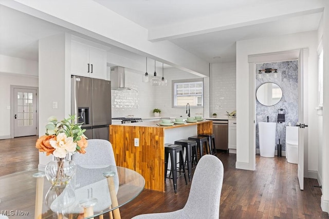 kitchen with decorative light fixtures, a center island, white cabinets, stainless steel appliances, and wall chimney range hood