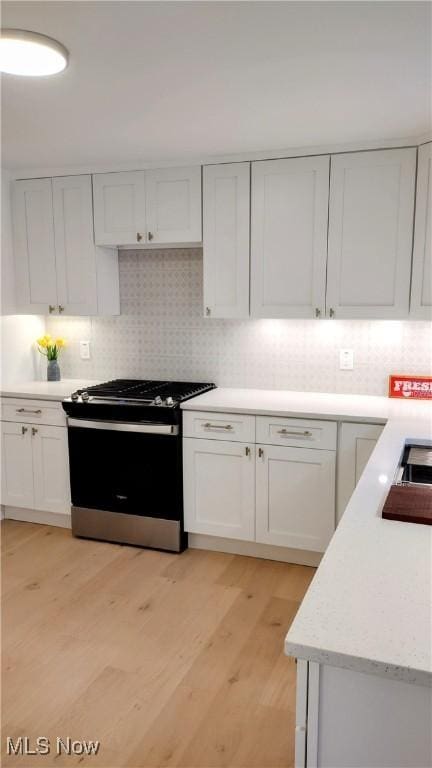 kitchen featuring white cabinetry, backsplash, light hardwood / wood-style flooring, and stainless steel range with gas stovetop