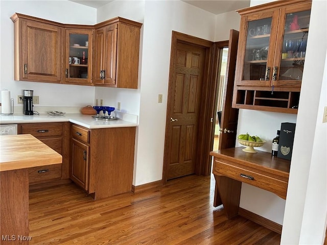 kitchen featuring light wood finished floors, brown cabinetry, butcher block counters, and glass insert cabinets