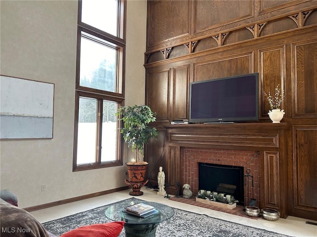 living area with a brick fireplace, baseboards, and a high ceiling