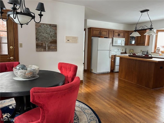 kitchen featuring brown cabinetry, white appliances, dark wood finished floors, and hanging light fixtures