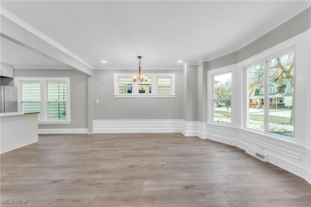 unfurnished dining area featuring ornamental molding, a chandelier, light wood-type flooring, and a wealth of natural light