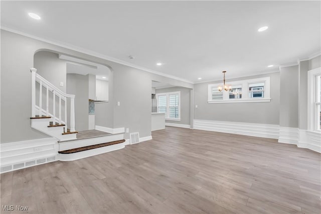 unfurnished living room with an inviting chandelier, ornamental molding, and light wood-type flooring