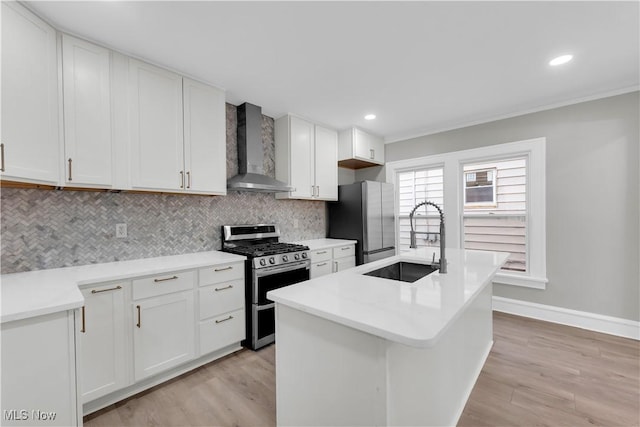 kitchen featuring appliances with stainless steel finishes, white cabinetry, sink, a center island with sink, and wall chimney exhaust hood