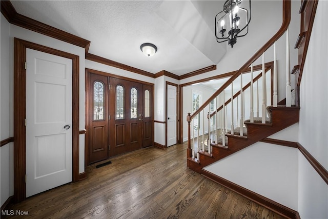 foyer featuring a textured ceiling, ornamental molding, dark hardwood / wood-style floors, and a chandelier