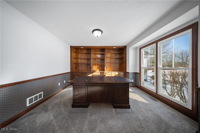 unfurnished office featuring dark colored carpet, a textured ceiling, and built in shelves