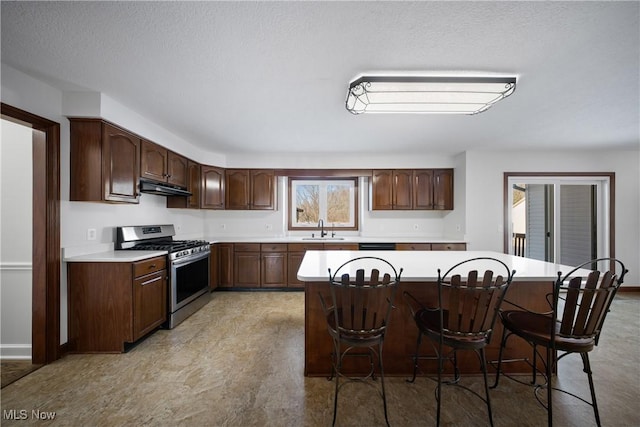 kitchen with dark brown cabinetry, sink, stainless steel range with gas cooktop, and a breakfast bar