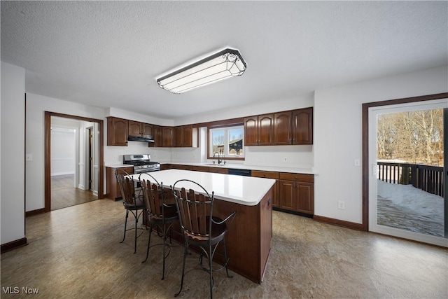 kitchen featuring sink, stainless steel gas stove, dark brown cabinets, a kitchen breakfast bar, and a kitchen island