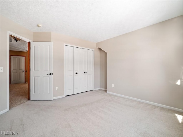 unfurnished bedroom featuring light carpet, a closet, and a textured ceiling