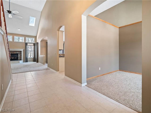 carpeted entrance foyer featuring ceiling fan, a stone fireplace, and high vaulted ceiling