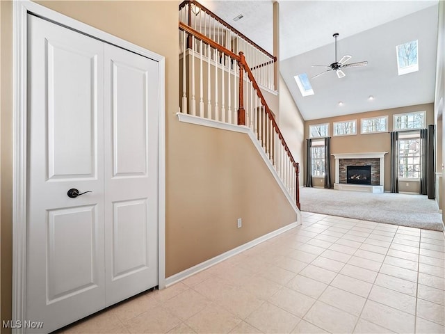 stairway featuring high vaulted ceiling, a fireplace, a skylight, ceiling fan, and tile patterned floors