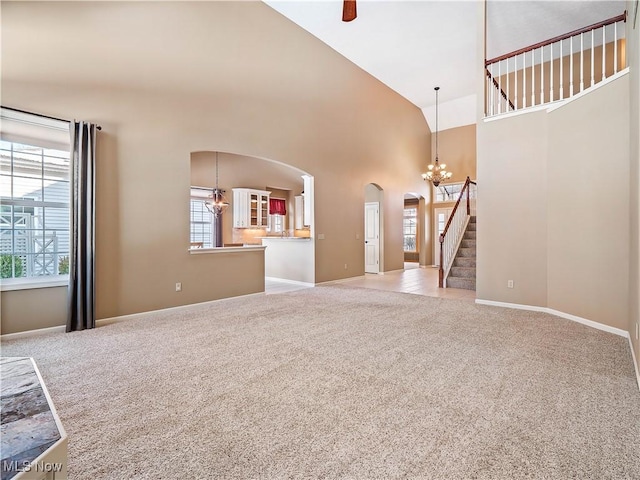 unfurnished living room with a chandelier, high vaulted ceiling, and light carpet