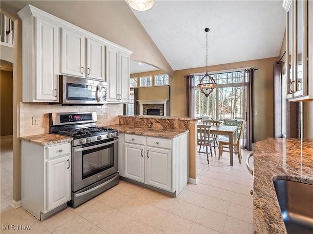 kitchen with lofted ceiling, stainless steel appliances, light stone countertops, white cabinets, and decorative light fixtures