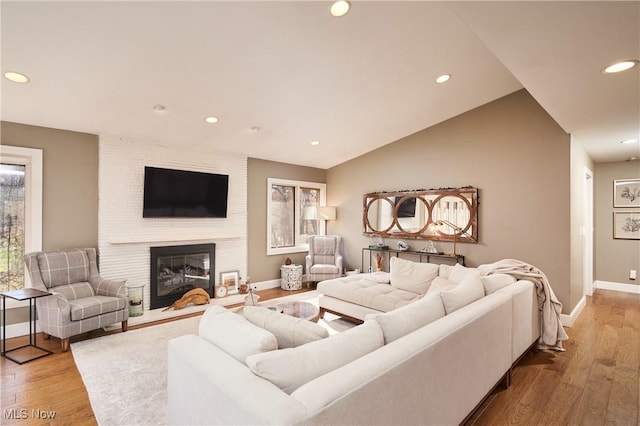 living room featuring lofted ceiling, a fireplace, and light hardwood / wood-style floors