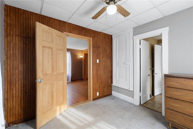 unfurnished bedroom featuring ceiling fan, carpet flooring, wooden walls, and a drop ceiling