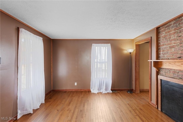 unfurnished living room with ornamental molding, a textured ceiling, a fireplace, and light hardwood / wood-style floors