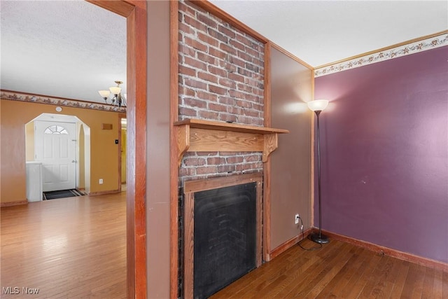 unfurnished living room featuring hardwood / wood-style flooring, ornamental molding, a brick fireplace, and a textured ceiling