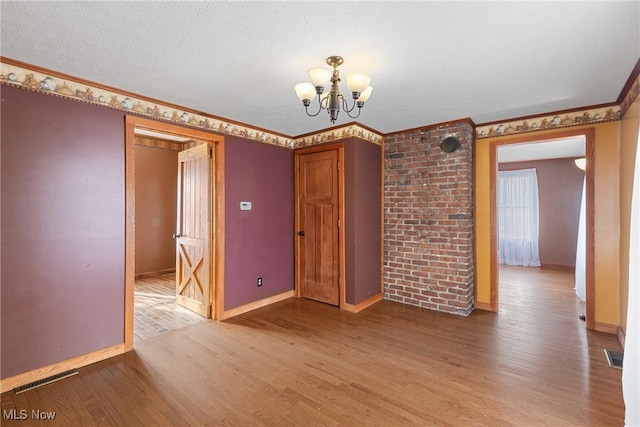 empty room featuring an inviting chandelier, ornamental molding, hardwood / wood-style floors, and a textured ceiling