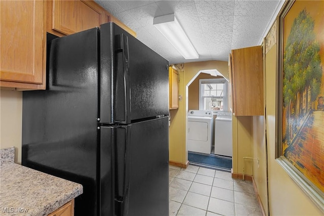 kitchen featuring black refrigerator, light tile patterned floors, washing machine and clothes dryer, and a textured ceiling