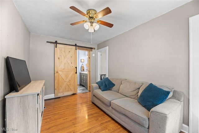 living room with ceiling fan, a barn door, and light hardwood / wood-style floors