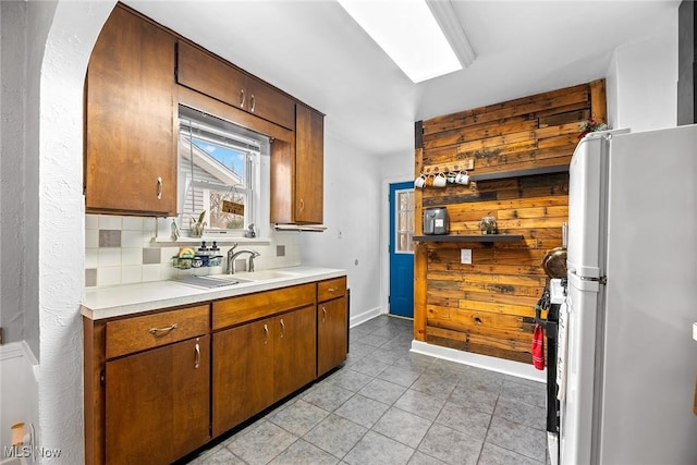 kitchen featuring light tile patterned flooring, a skylight, sink, decorative backsplash, and white fridge