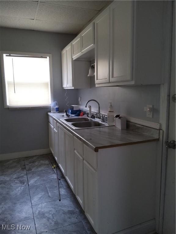 kitchen with a paneled ceiling, sink, and white cabinets