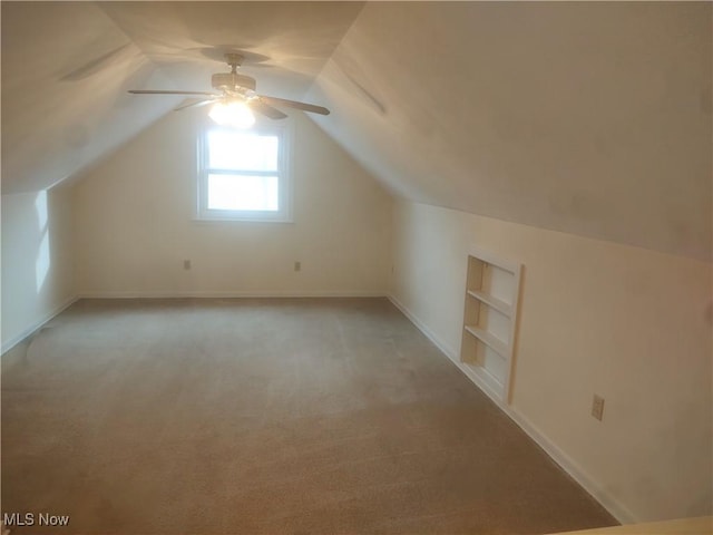 additional living space with built in shelves, light colored carpet, lofted ceiling, and ceiling fan