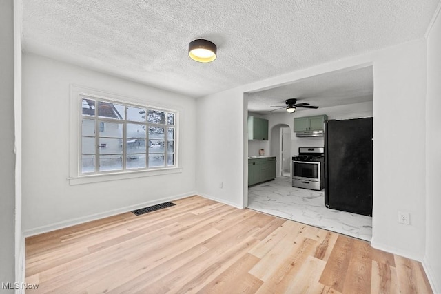 kitchen with green cabinets, stainless steel gas stove, light hardwood / wood-style floors, a textured ceiling, and black fridge