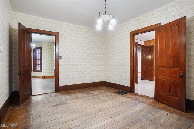 spare room with wood-type flooring and an inviting chandelier