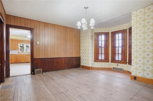 spare room featuring an inviting chandelier, a textured ceiling, and light hardwood / wood-style floors