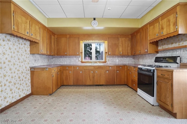 kitchen with a drop ceiling, backsplash, sink, and gas stove