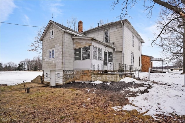 snow covered back of property featuring a sunroom