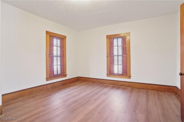 unfurnished room featuring plenty of natural light, a textured ceiling, and light wood-type flooring