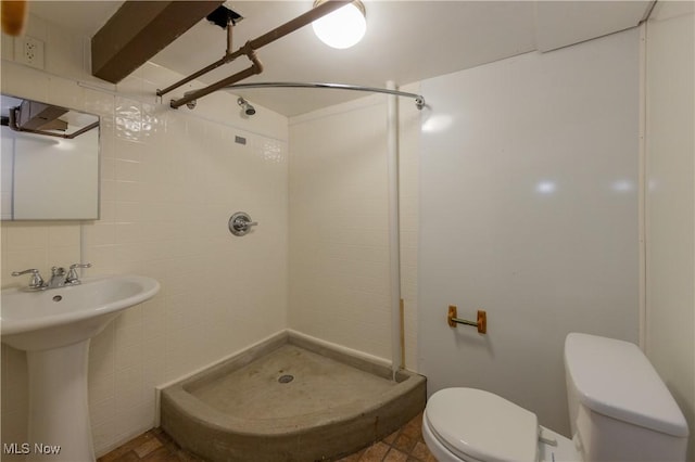 bathroom featuring tiled shower, toilet, sink, and tile walls